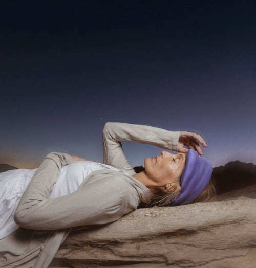 Person lying on a rock with a purple headband against a clear sky