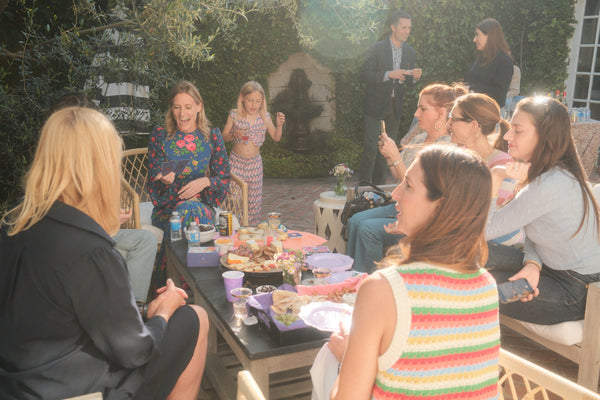 Group of people gathered around a table outdoors, possibly at a party or gathering.