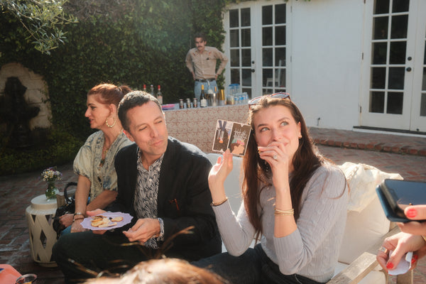 People sitting outdoors, one holding a photo, with a casual setting.